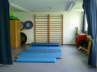 Die Sporthalle des Kindergartens. Auf dem Boden liegen blaue Matte, an der Wand gegenüber befinden sich Klettergerüste.