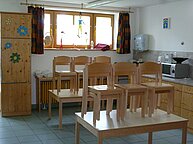 Ein Aufenthaltsraum des Kindergartens. Stühle stehen ordentlich aufgeräumt auf den Tischen.