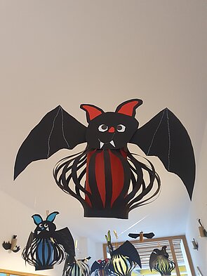 Ein Bild von einer von Kindern gebastelten, schwarzen Fledermaus, mit Fangzähnen und einem roten Bauch.