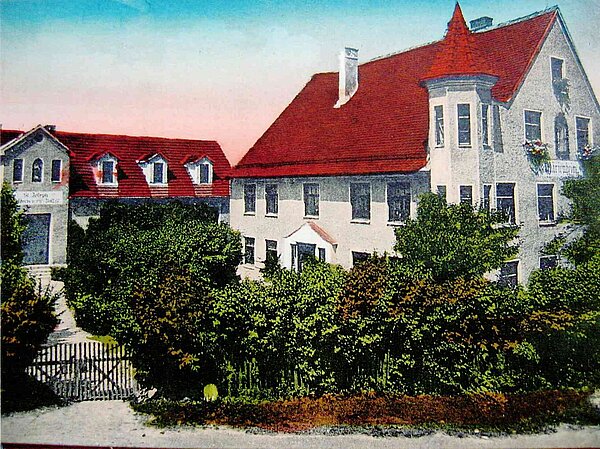 Das Bild zeigt das alte Gebäude des Kindergarten Merchings, ein großes Haus mit rotem Dach und einem Türmchen.