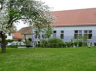 Außenansicht des Gebäudes mit Grünflächen und Schaukeln.