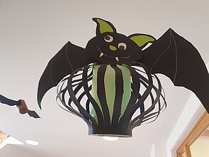 Ein Bild von einer von Kindern gebastelten, schwarzen Fledermaus, mit Fangzähnen und einem grünen Bauch.
